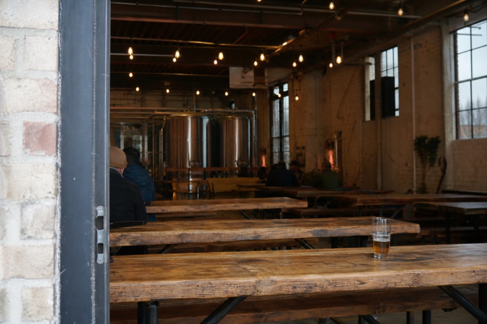 Interior of a craft brewery taproom with long wooden tables and brewing equipment
