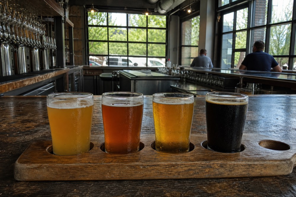 Flights of beer sampled on a bar top with water views beyond the window