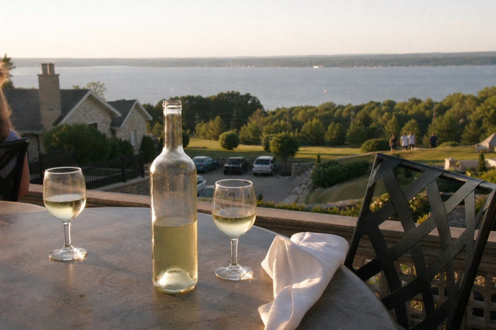 An open bottle of white wine and glasses on a winery terrace overlooking a lake