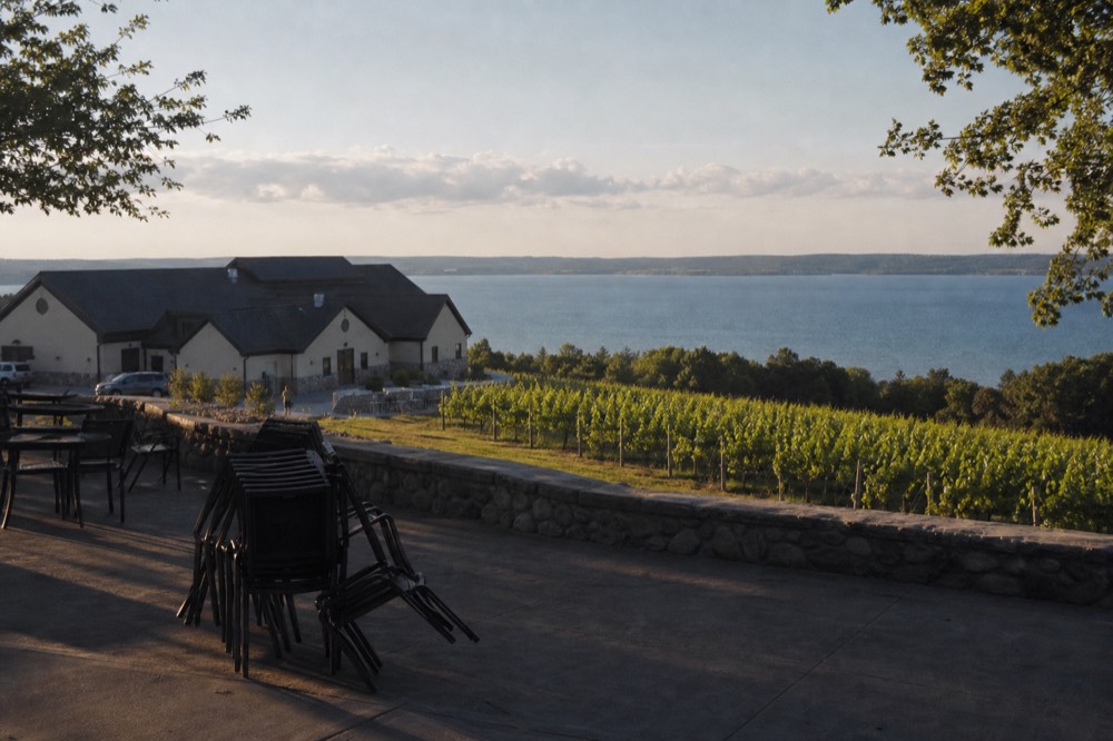 A vineyard estate building with a tasting room patio above rows of vines