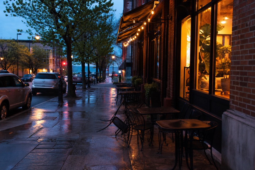 A downtown Traverse City storefront with a lit sign and sidewalk tables at dusk