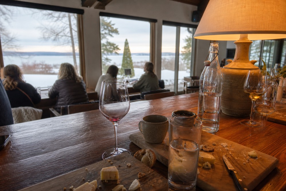 Warm-lit interior of a tasting room bar with snow visible through the windows